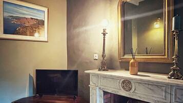 A room with a fireplace, a framed mirror, a television on a wooden stand, and a framed picture on the wall.