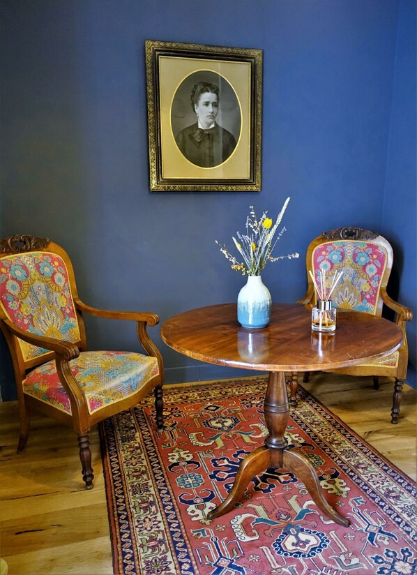 A room with a round wooden table, two upholstered chairs with floral upholstery, a vase with flowers, and a framed portrait on the wall. - À Villa di Rutali (Rutali)