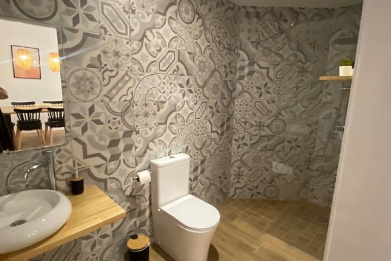 A bathroom with patterned tiles, a white toilet, a wooden vanity with a sink, and a small trash bin.