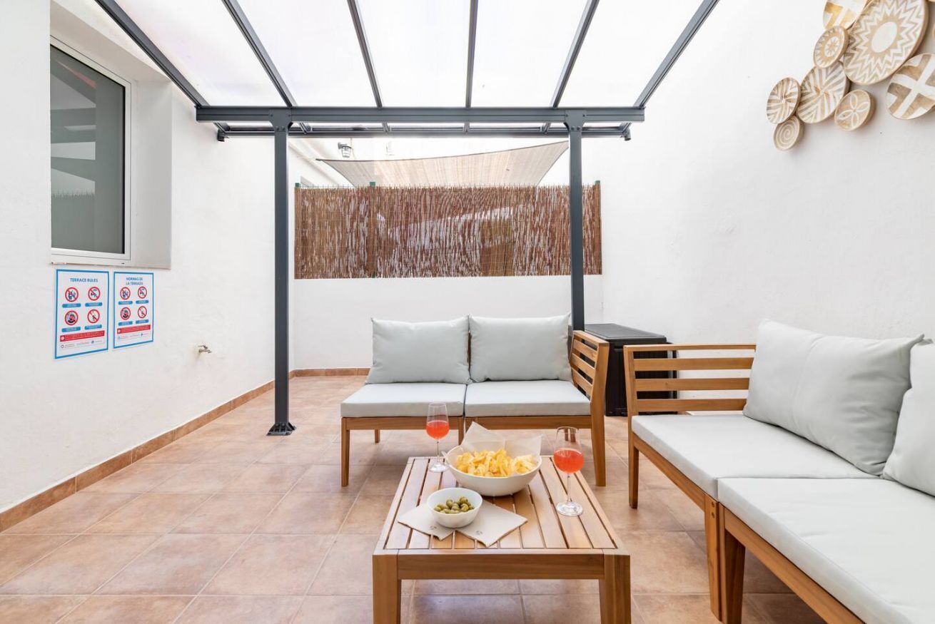 A modern patio area with a wooden table, two sofas, and a dining table set with snacks and drinks.