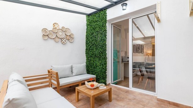 A modern patio with a wooden sofa, a small table with a bowl and a glass, and a green vertical garden. - A (VA080-5) TH Bioparc con Terraza Apartment E (Valencia / València)