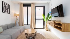 A modern living room with a grey sofa, a round coffee table, a TV mounted on the wall, and a large window with curtains. - A (VA080-5) TH Bioparc con Terraza Apartment E (Valencia / València)
