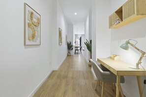 A hallway with a desk, chair, lamp, and wall-mounted shelf with a teddy bear.