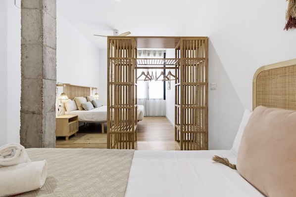 Ein Hotelzimmer mit Bett, einer Holzablage, einer Kleiderstange und Blick auf ein weiteres Zimmer.