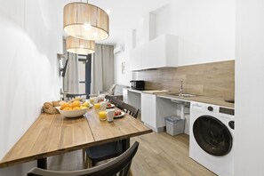 A compact kitchen with a wooden dining table, a washing machine, and a hanging light fixture.