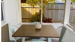 Een overdekt terras met een houten tafel en vier lichtblauwe stoelen.