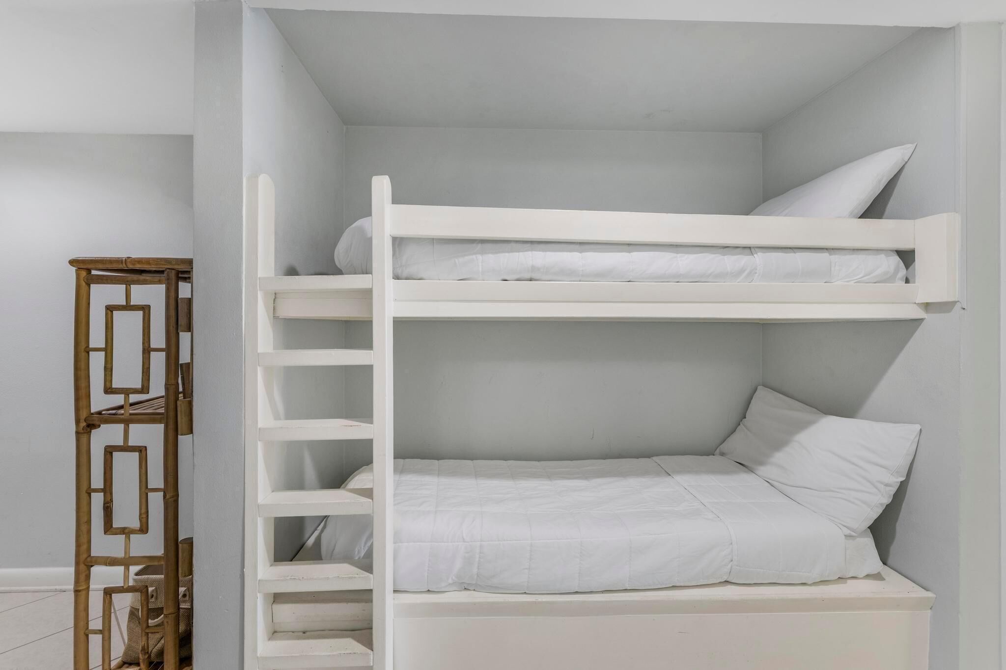 Una cama litera con ropa de cama blanca en una habitación con paredes blancas y una escalera de madera.