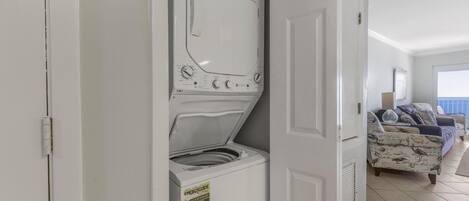 Un lavadero con lavadora y secadora de carga frontal, una puerta que da a una sala de estar con un sofá estampado y vistas al exterior.
