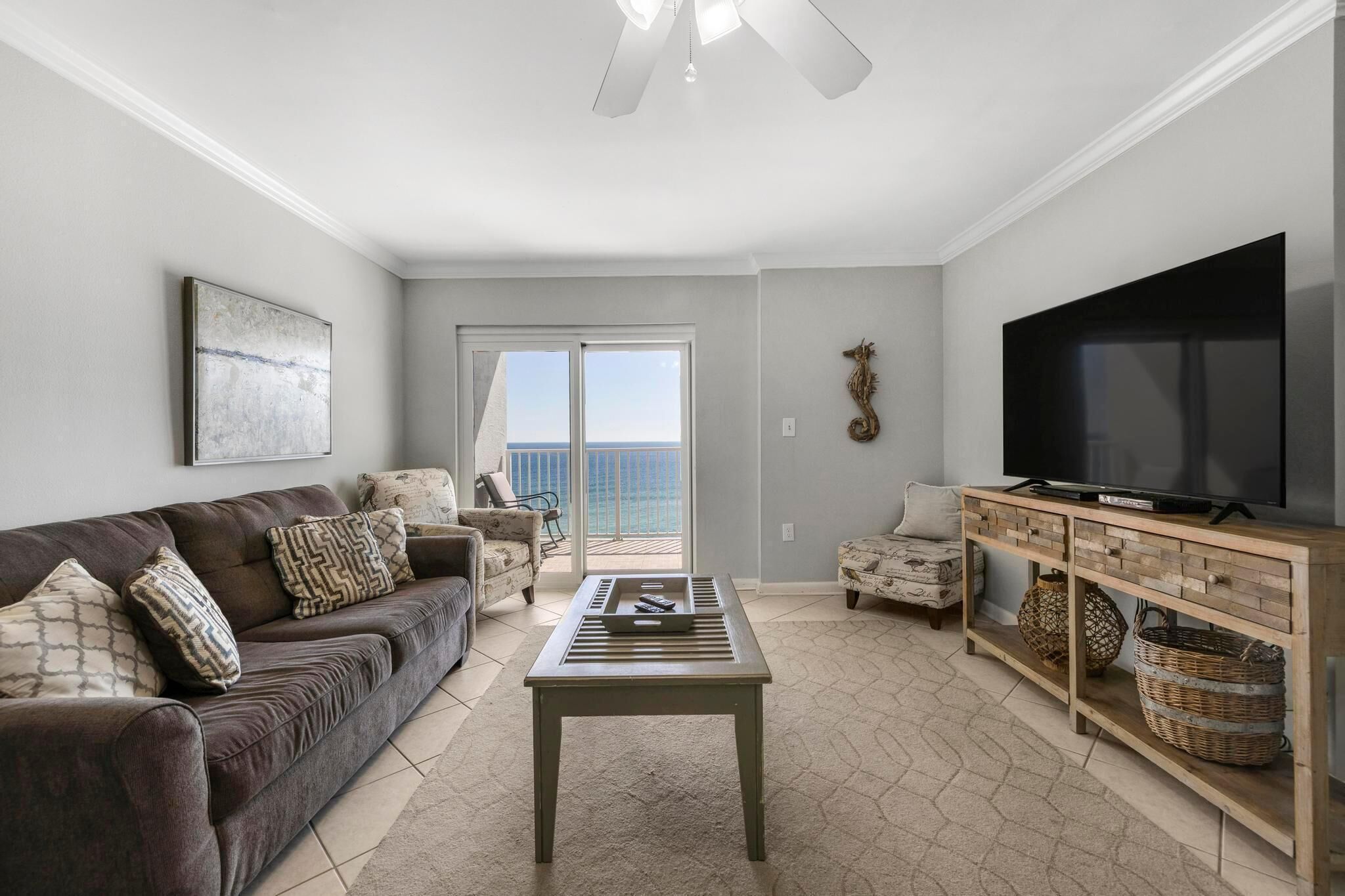 A living room with a sofa, coffee table, TV, and a view of the ocean through a sliding door.