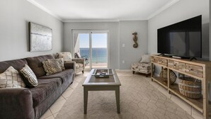 A living room with a sofa, coffee table, TV, and a view of the ocean through a sliding door. - Westwind 802 (Gulf Shores)