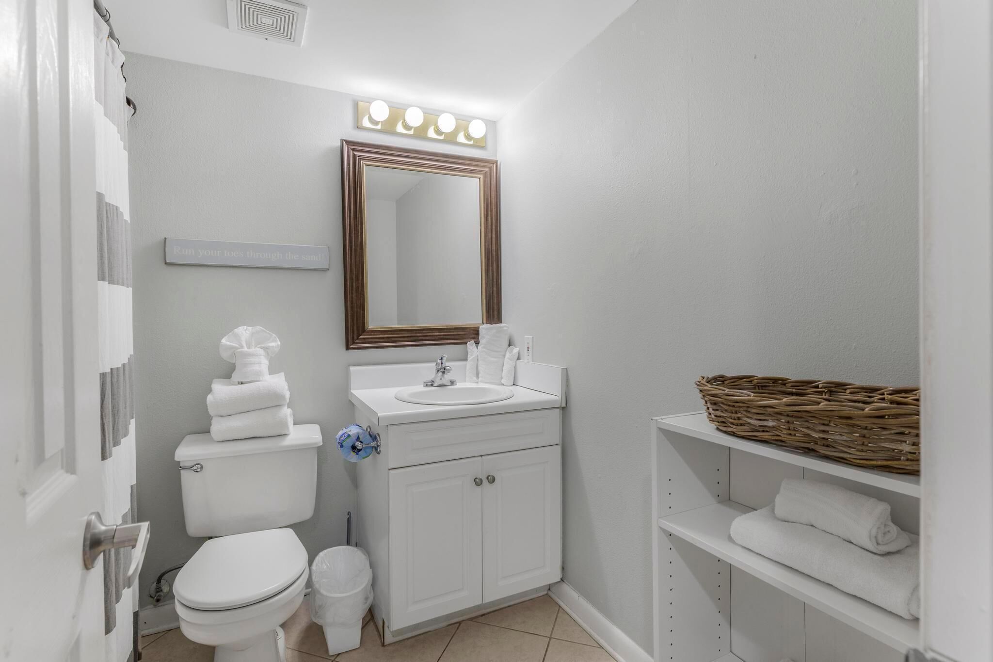 A bathroom with a toilet, sink, mirror, and shelves with towels.