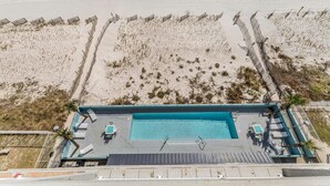 An aerial view of a beachside hotel with a swimming pool, lounge chairs, and a fenced beach area. - Westwind 802 (Gulf Shores)