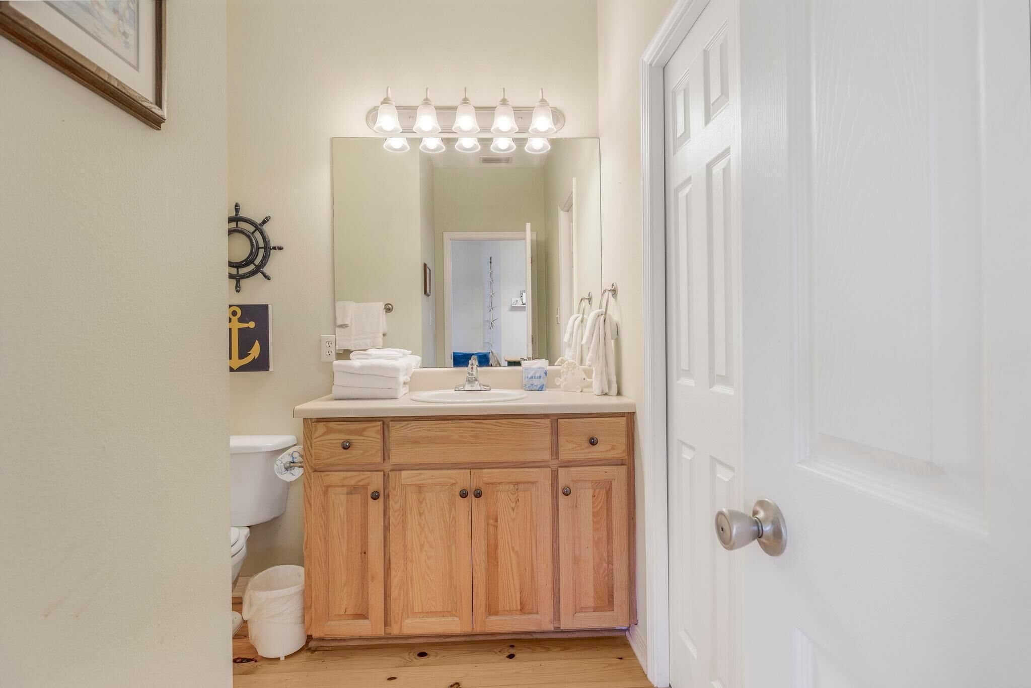 A bathroom with a wooden vanity, a sink, a mirror with lights, a toilet, and a door.