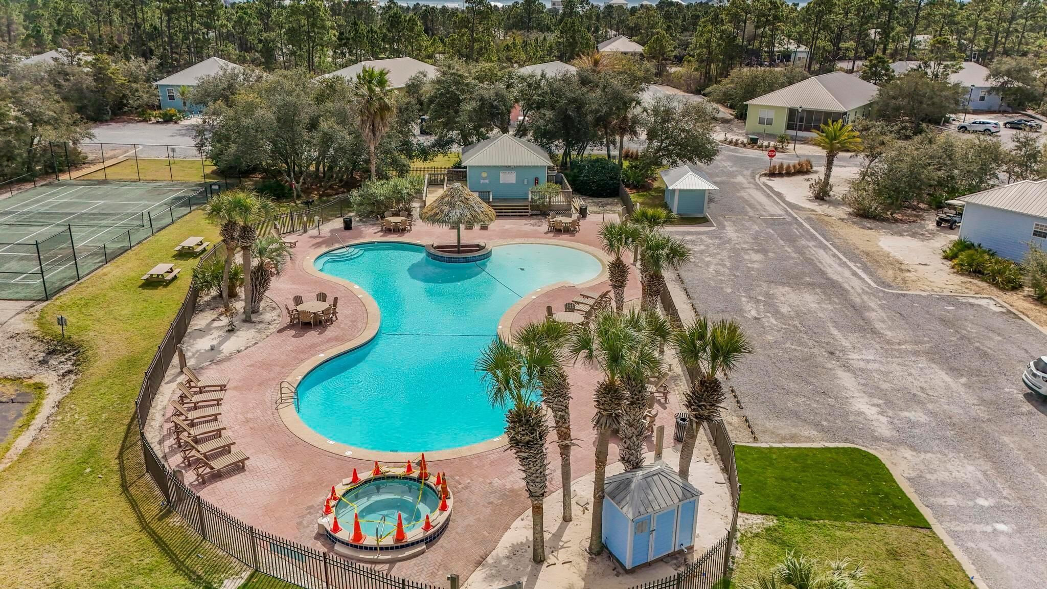 A large, curved swimming pool surrounded by palm trees and lounge chairs, with a small hot tub and a gazebo in the center.