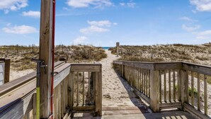 Ein hölzerner Steg führt zu einem Strand unter blauem Himmel.