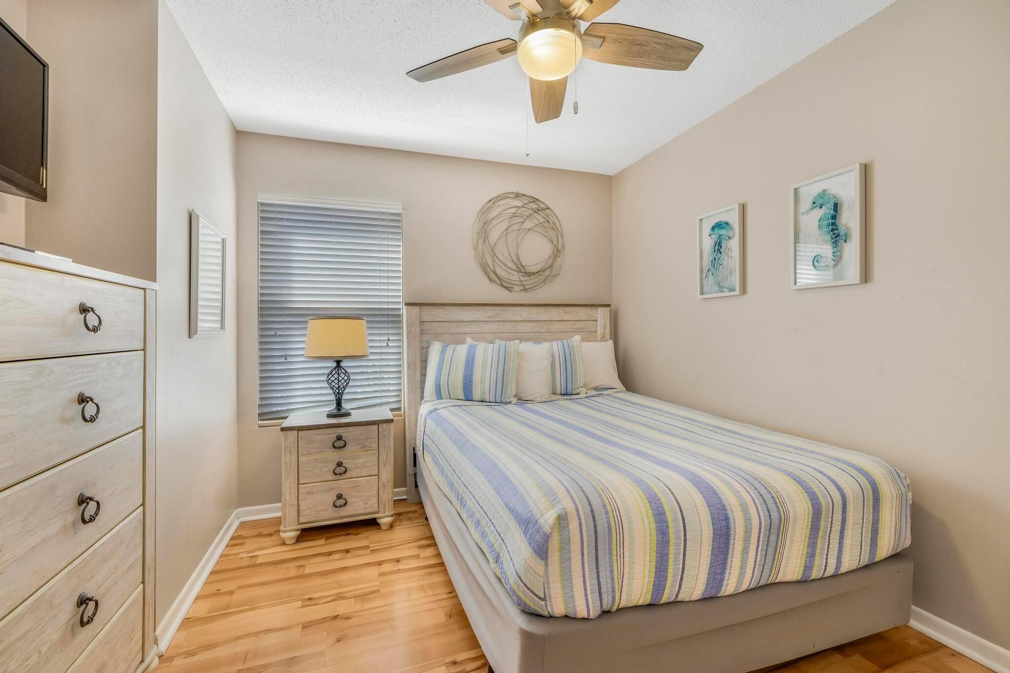 Un dormitorio con cama, mesita de noche, cómoda, ventilador de techo y decoración en la pared.