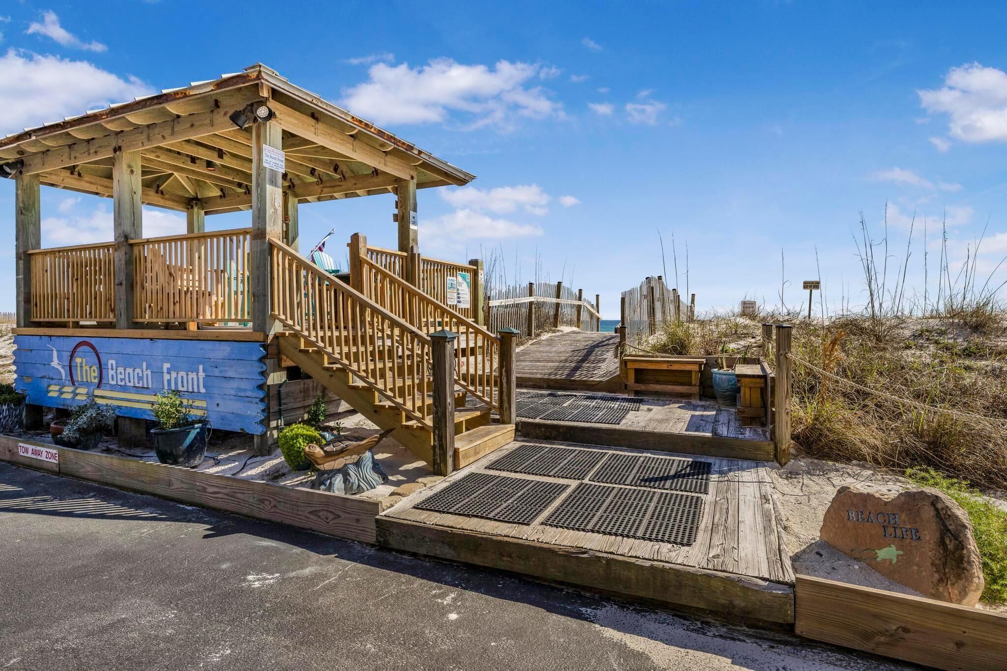 A wooden beach hut with a sign reading "The Beach Front" and a "Beach Life" sign on a rock.
