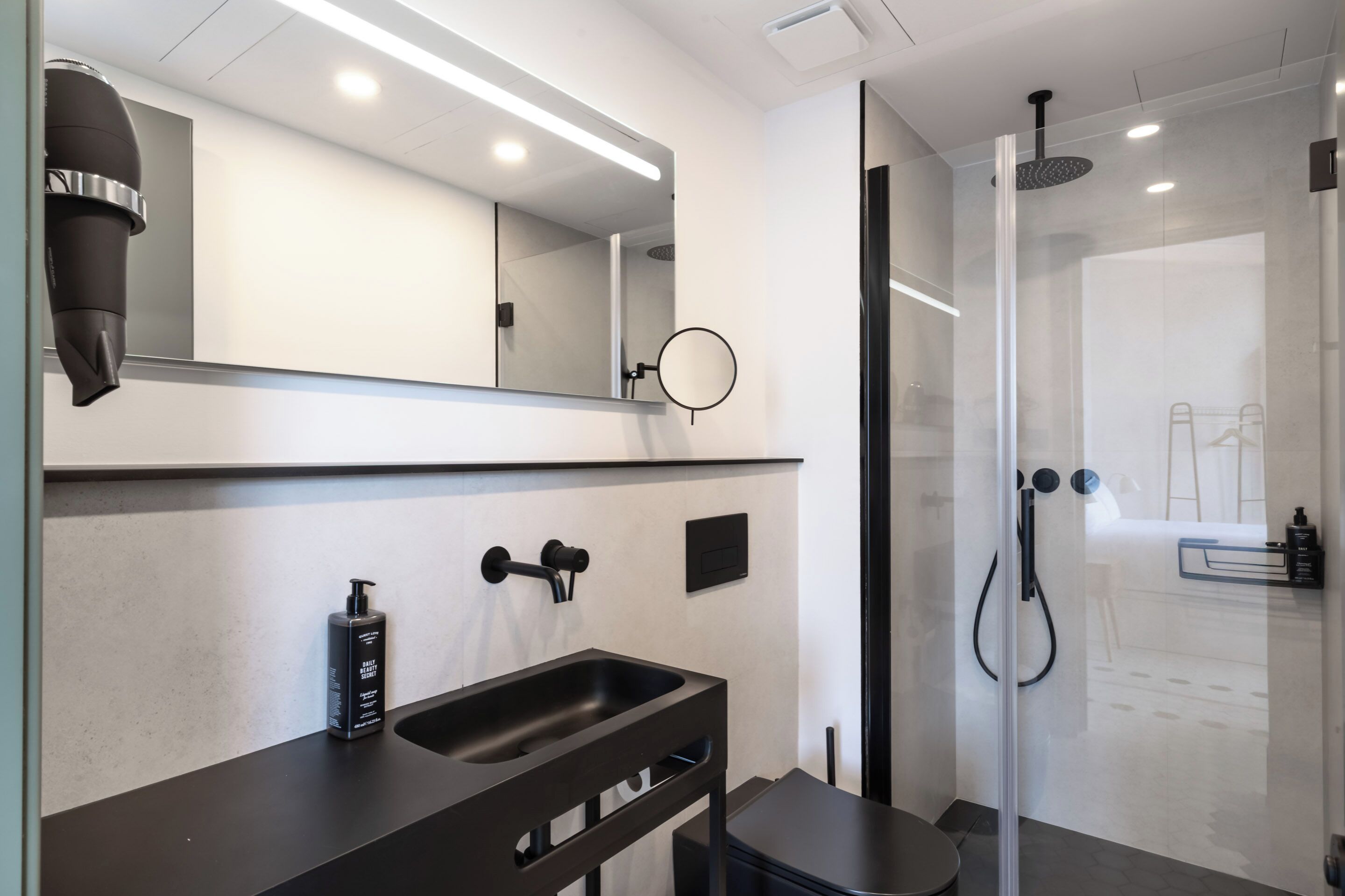 A modern bathroom with a large mirror, a black sink, a handheld showerhead, and a glass-enclosed shower.