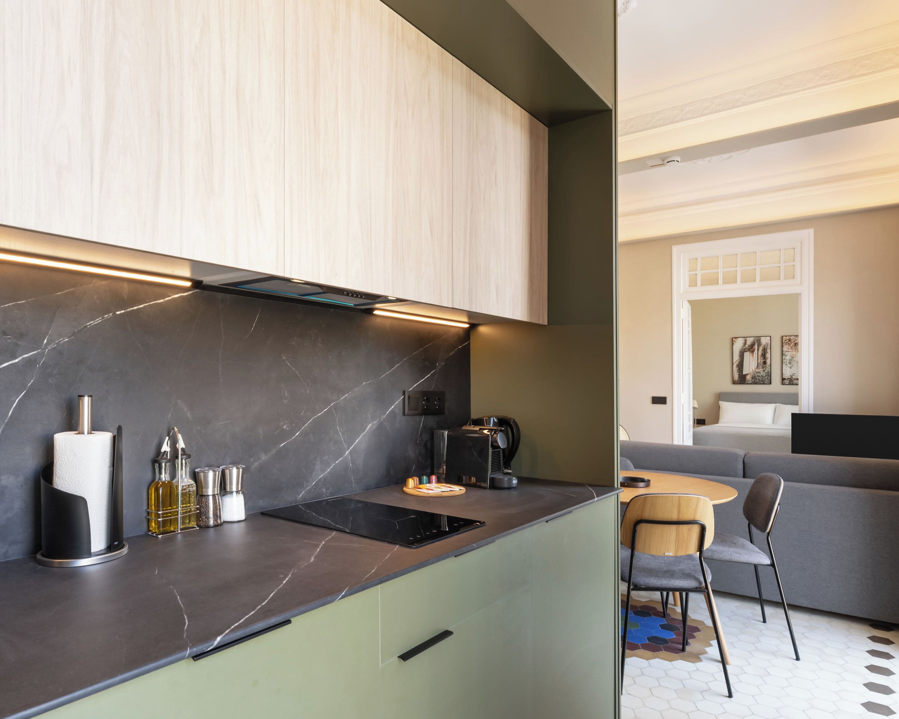 A modern kitchen with a marble countertop, a built-in stove, and a coffee machine. There is a dining area with a round table and two chairs.