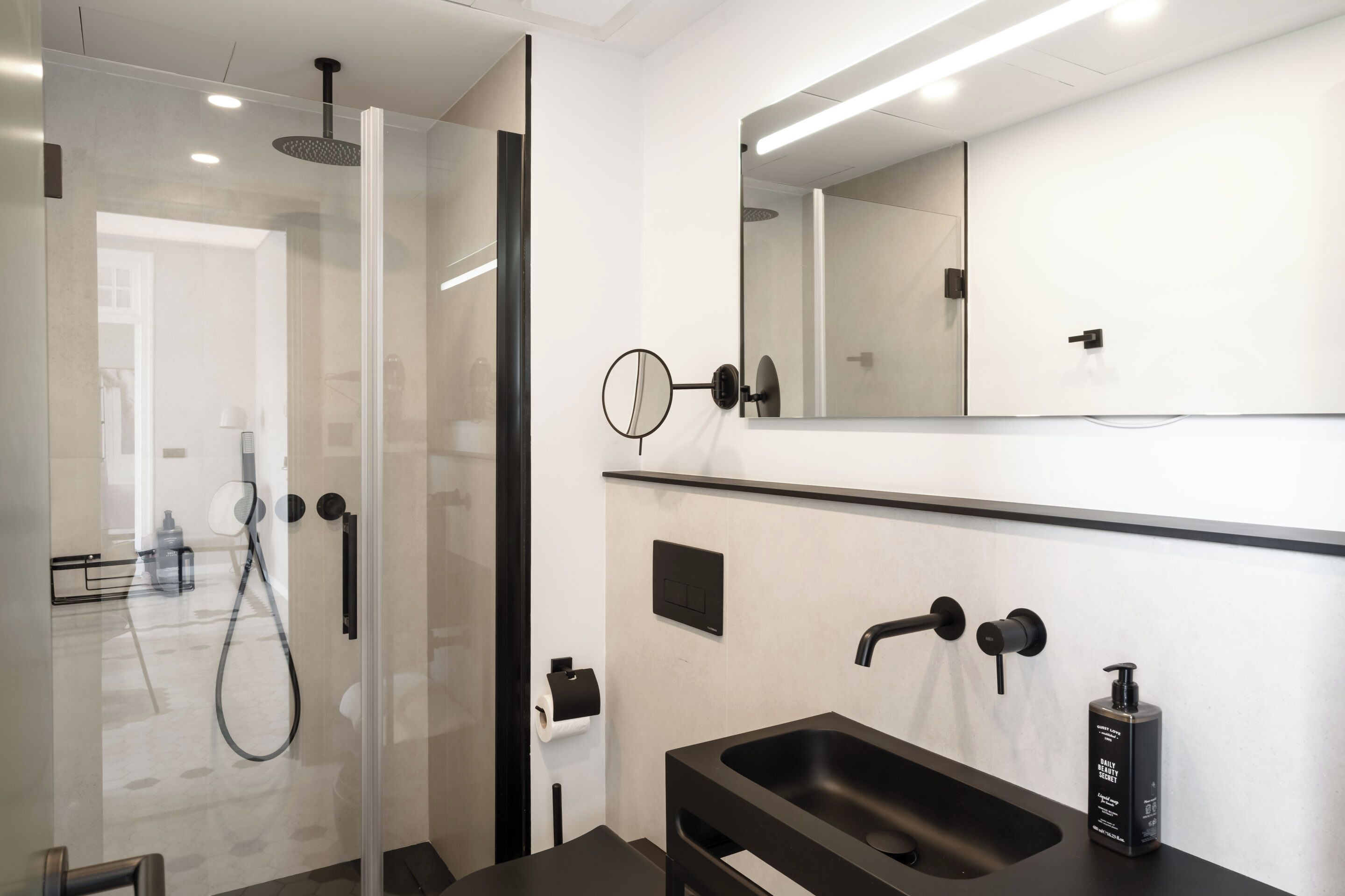 Un baño moderno con ducha de vidrio, lavabo negro y espejo grande.