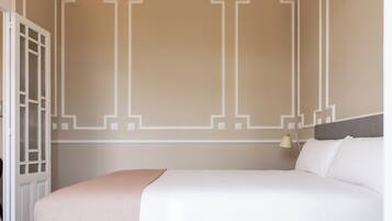 Habitación de hotel ordenada con una cama grande, una mesita de noche y una puerta con paneles de vidrio.