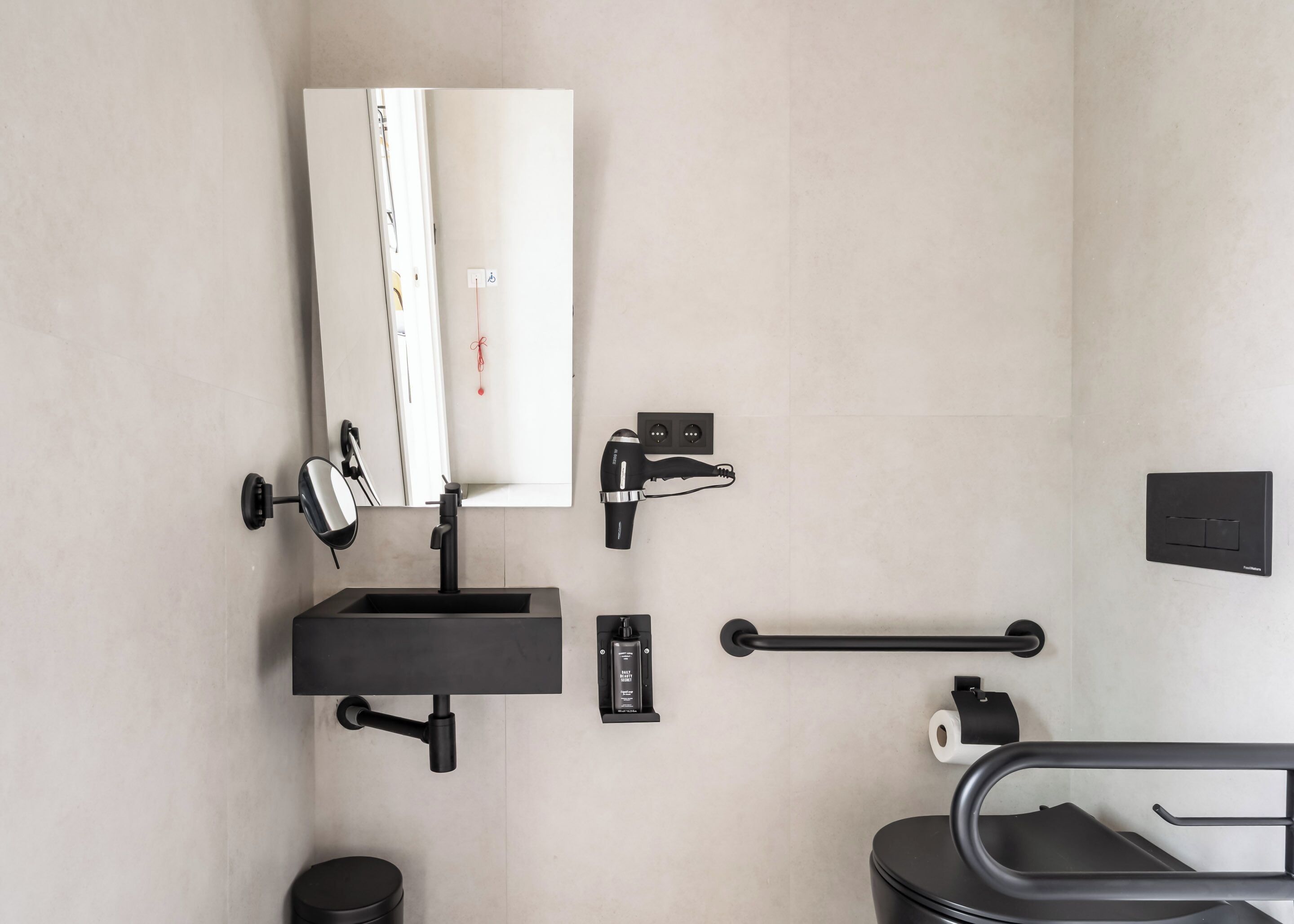 Et moderne badeværelse med vask, spejl, håndklæderække, hårtørrer og toiletpapirsholder.