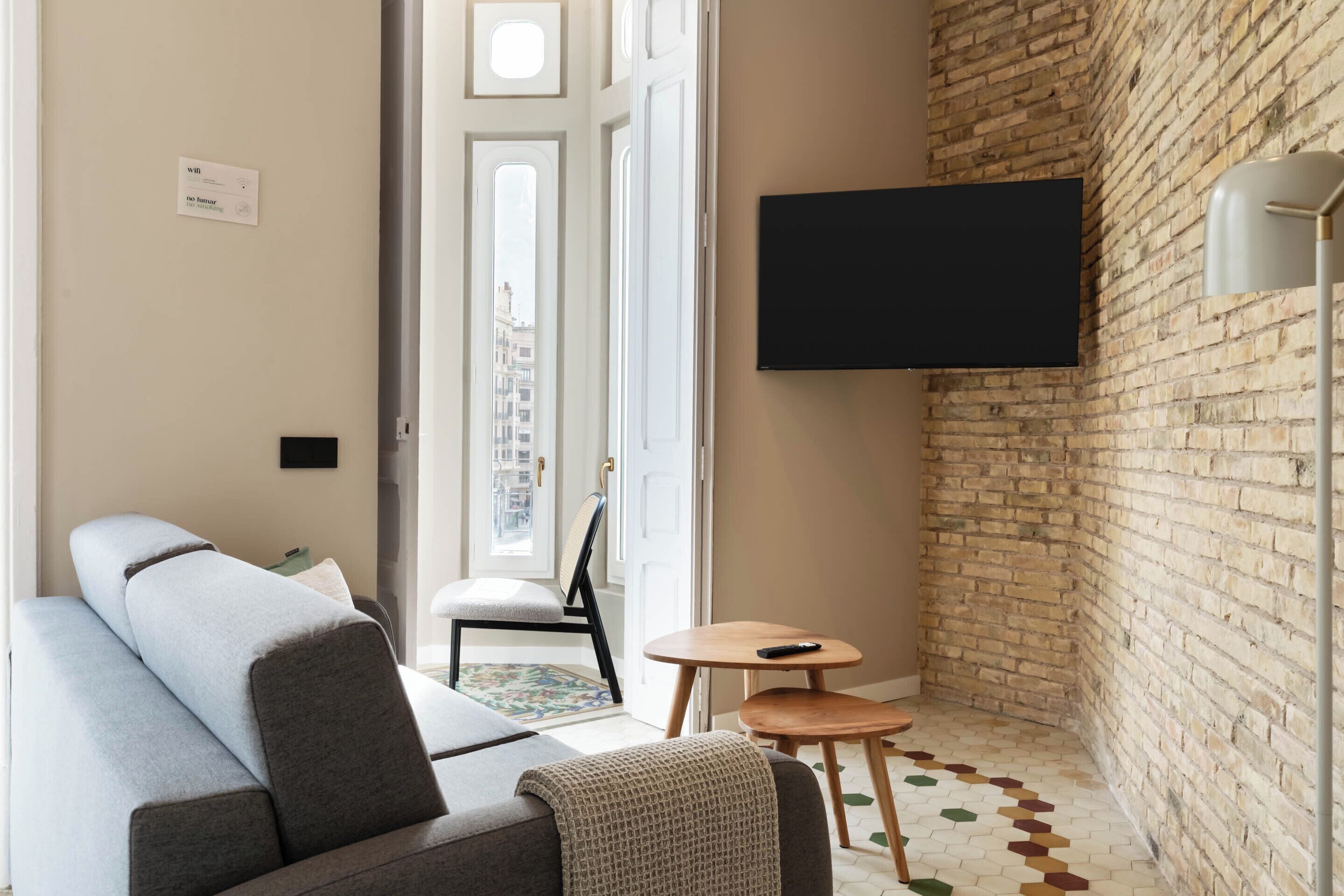 Una sala de estar moderna con un sofá, una mesita y un televisor instalado en una pared de ladrillo.