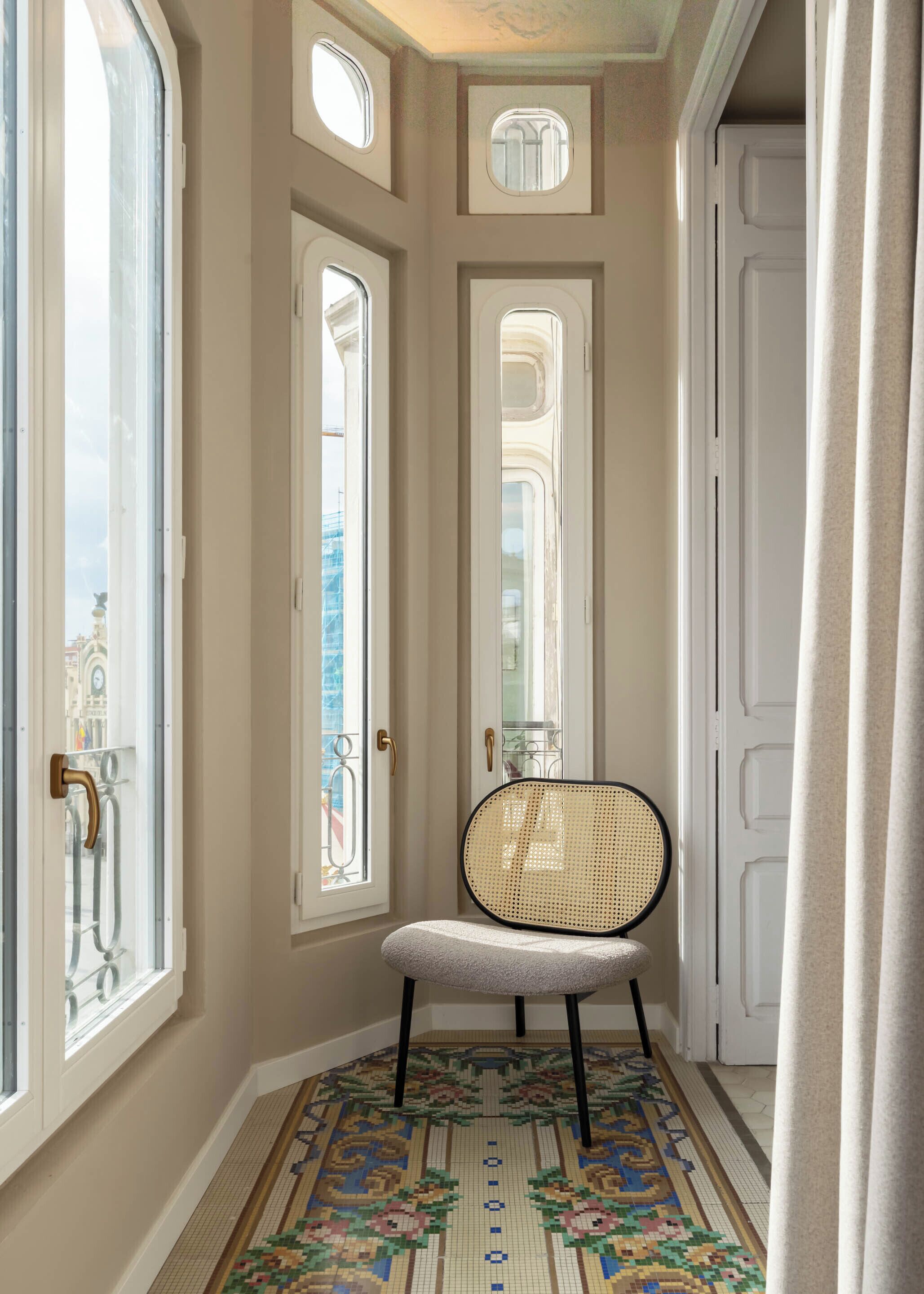 Un pasillo con piso estampado, una silla de ratán y una puerta con ventanal.