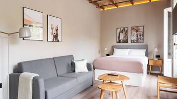 Een moderne slaapkamer met een grijze bank, een bed met een roze deken, houten nachtkastjes en ingekaderde foto's aan de muur.