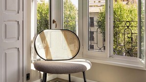 Une pièce avec une chaise près d’une grande fenêtre, un sol à motifs et une vue sur les bâtiments et les arbres à l’extérieur.