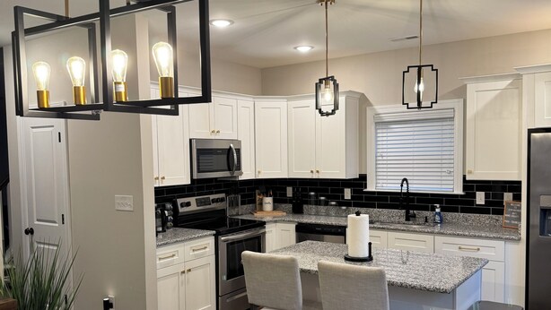 Una cocina moderna con armarios blancos, una isla central con taburetes altos, un refrigerador de acero inoxidable y un microondas.