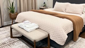 Un dormitorio moderno con una cama, un banco y una planta en maceta.