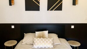 A neatly arranged bedroom with a large bed, two wall-mounted artworks, and two small round tables.