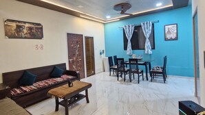 A modern living room with a sofa, coffee table, dining table, and chairs. - Indraprastha villa (Mawal)