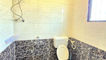 A bathroom with a toilet, a shower, and a hand dryer. There is a bucket on the floor.