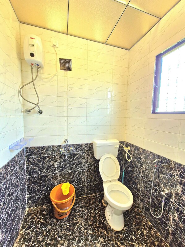A bathroom with a toilet, a shower, and a hand dryer. There is a bucket on the floor. - Indraprastha villa (Mawal)