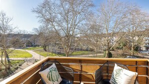 A wooden deck with two black chairs and a table, overlooking a park and residential area. - Troja Living - Apartment Helena am Park in the middle of Bruchsal (Bruchsal)