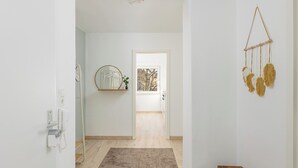 A hallway with a wooden floor, a round mirror on a shelf, a wall-mounted macrame piece, and a door leading to another room. - Troja Living - Apartment Helena am Park in the middle of Bruchsal (Bruchsal)