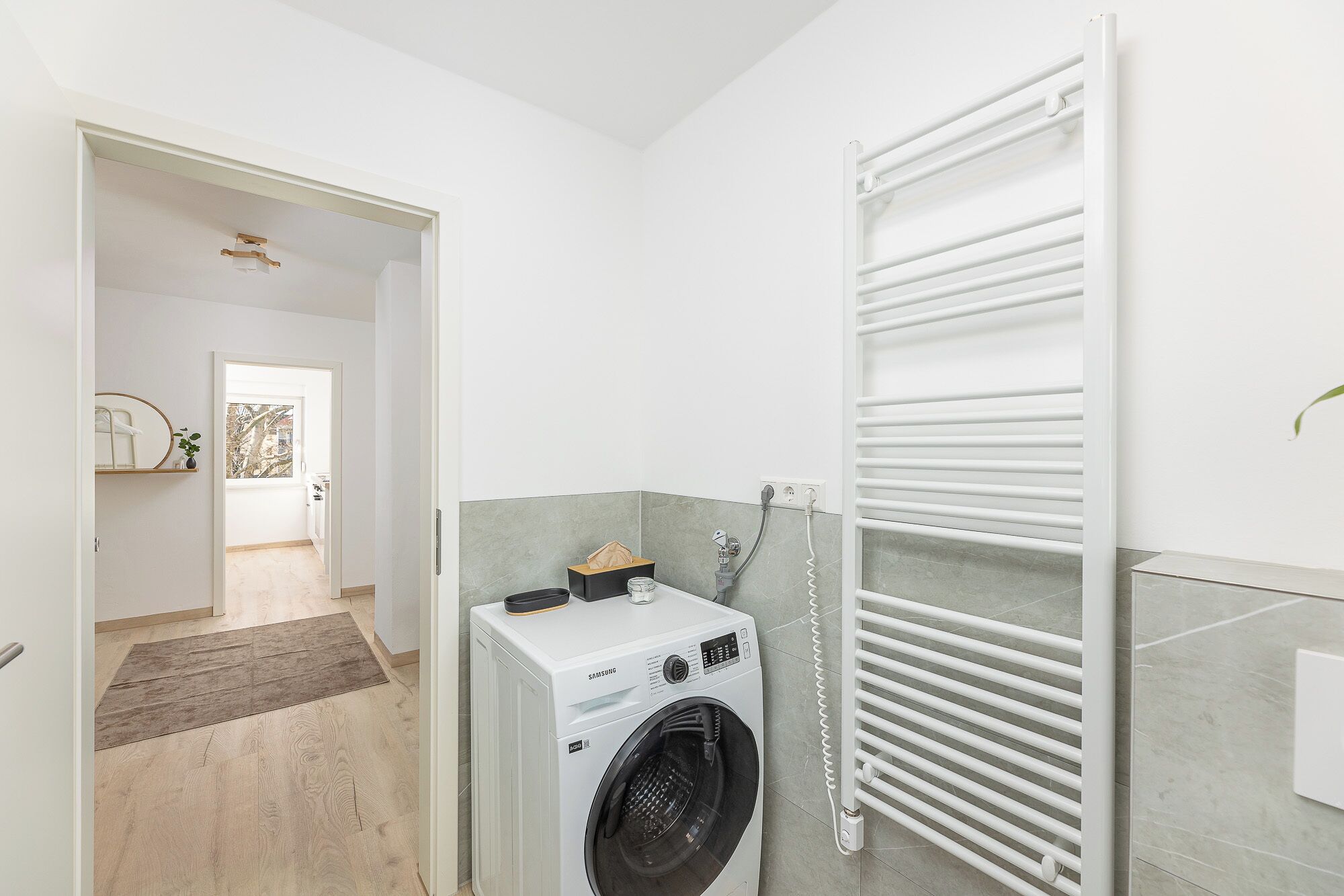 Une buanderie équipée d’un lave-linge à chargement frontal, d’un porte-serviettes et d’un mur recouvert de carreaux.