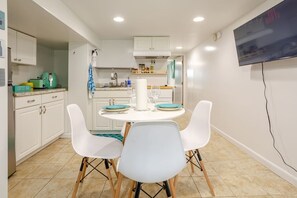 Une cuisine compacte avec des meubles blancs, un coin café et un espace repas comprenant une table ronde et des chaises blanches.