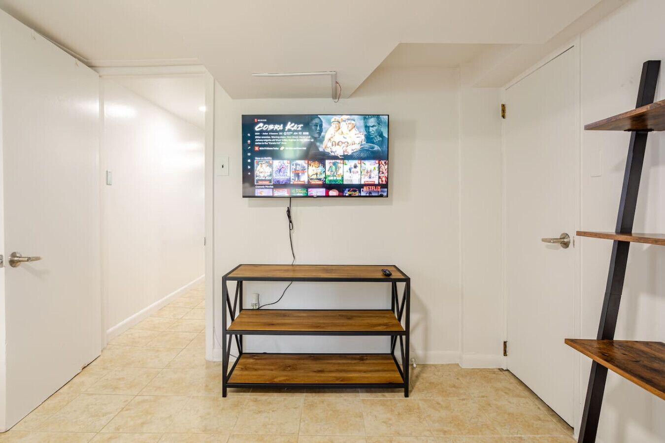 A room with a mounted TV displaying a movie, a wooden shelf unit, and white doors.
