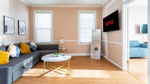 Un salon moderne avec un canapé gris, une table basse ronde et un téléviseur fixé au mur.