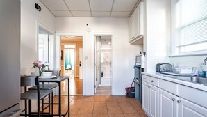 Une cuisine avec des meubles blancs, un coin repas avec une table et des chaises, et une vue sur une autre pièce.