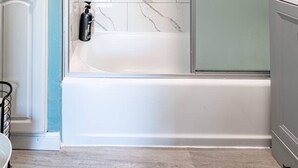 Une salle de bain dotée d’une douche à parois de verre, de carreaux de marbre blanc et d’une baignoire blanche.