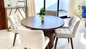 A modern dining area with a round table, four upholstered chairs, and a potted plant.