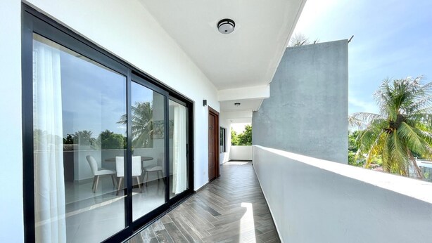 A modern corridor with a glass door leading to a balcony with a view of palm trees.