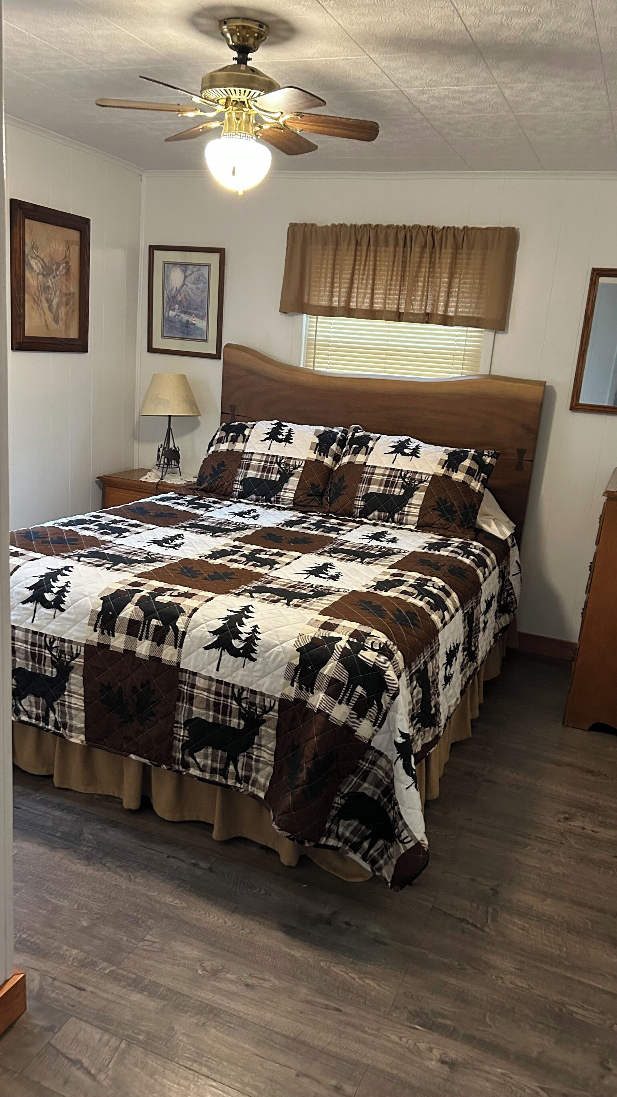 Una camera da letto con un letto, una ventola a soffitto, una finestra con persiane e un quadro appeso al muro.