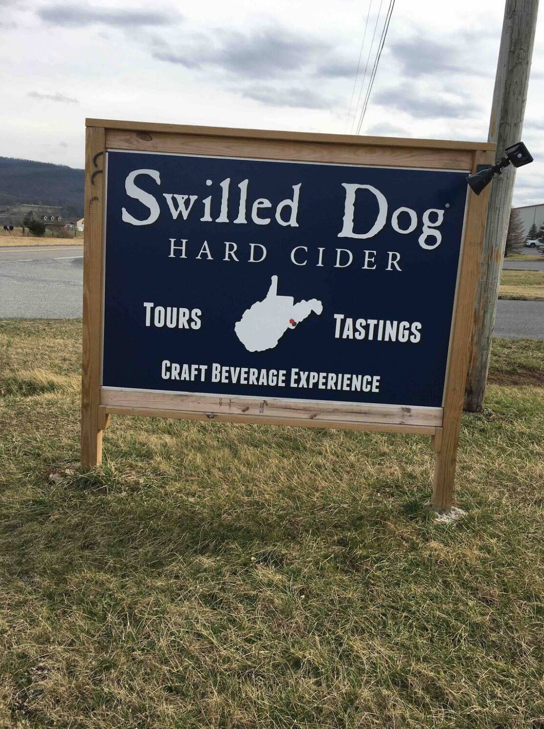 A signboard for Swilled Dog Hard Cider offering tours and tastings.