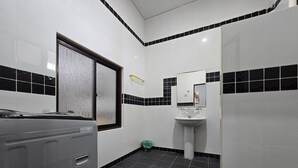 Een badkamer met een wit wastafelblad, zwart-wit tegels, een raam met geëtste glas en een groene prullenbak.