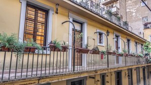 Une rangée de bâtiments jaunes dotés de balcons, chacun orné de plantes en pot et muni d’une rambarde en métal.